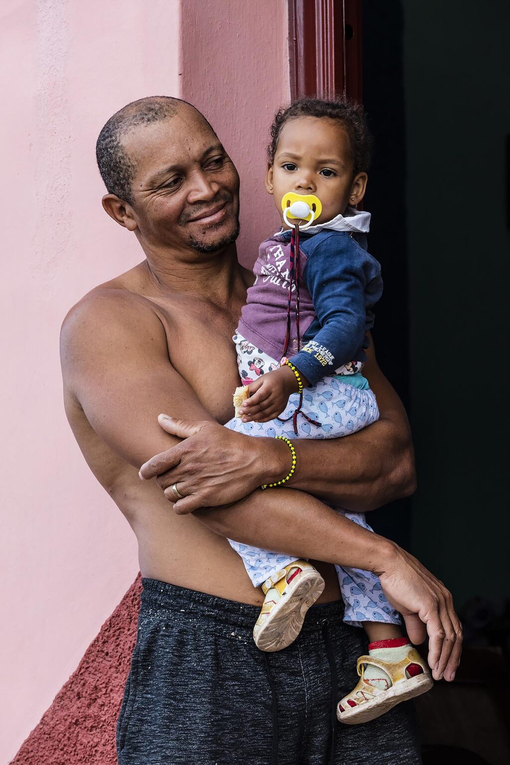A FATHER holds his baby daughter in a doorway - TRINIDAD, CUBA
