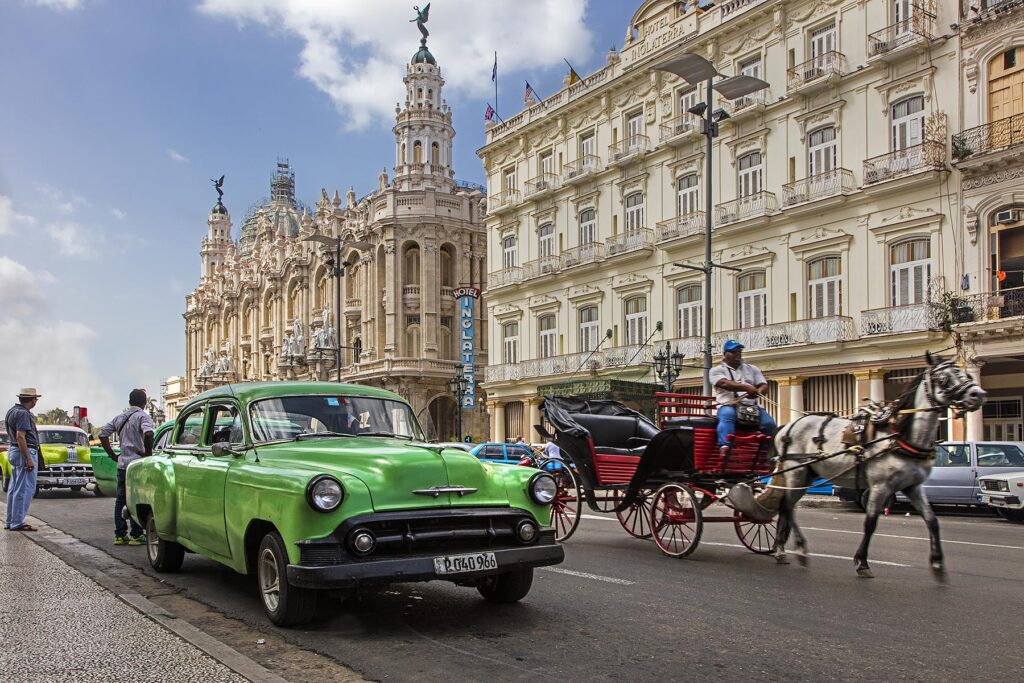 Classic American cars drive by in front of the HOTEL INGLATERRA LA TARAZZA and GRAND TEATRO DE HABANA along the PASEO DE MARTI  - HAVANA, CUBA