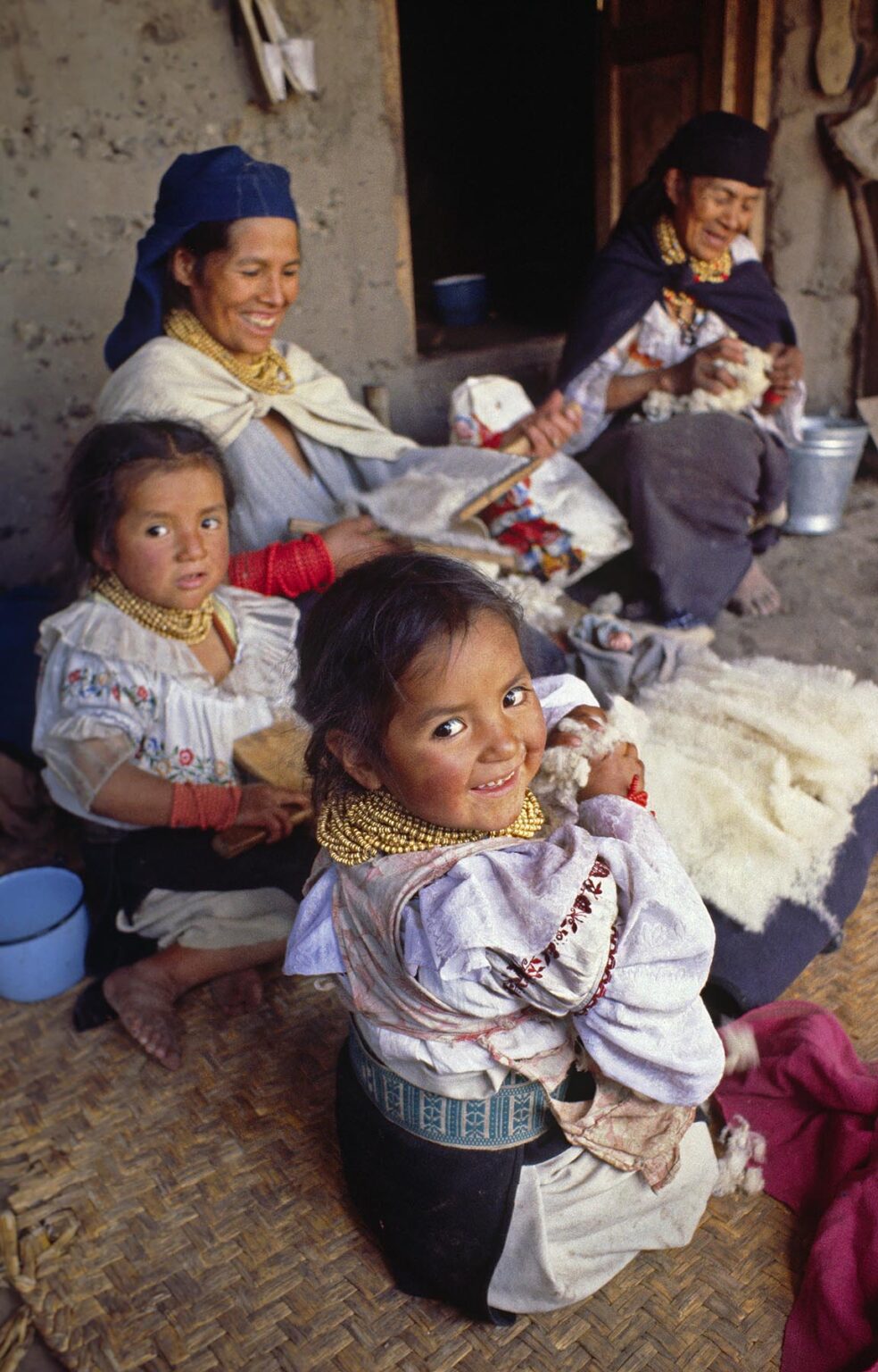 OTAVALO INDIAN WOMAN with FAMILY CARDING WOOL in the MARKETPLACE - OTAVALO, ECUADOR