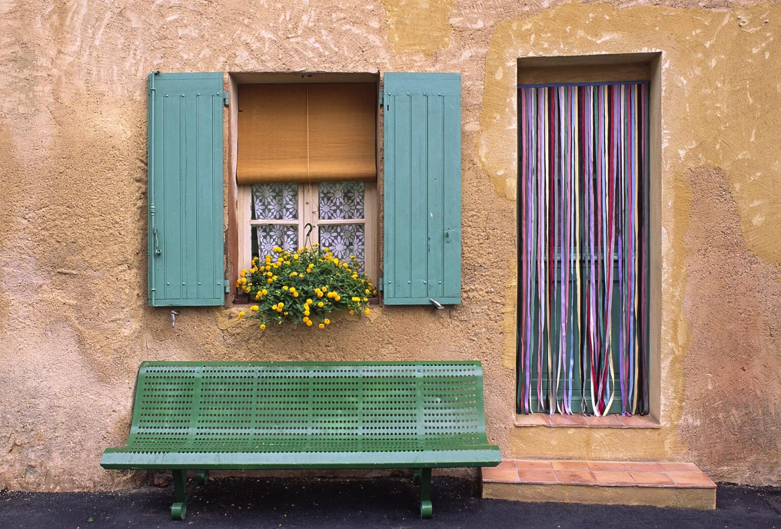Green bench and window shutters with flowering plant in the Village of ROUSSILLON - PROVENCE, FRANCE