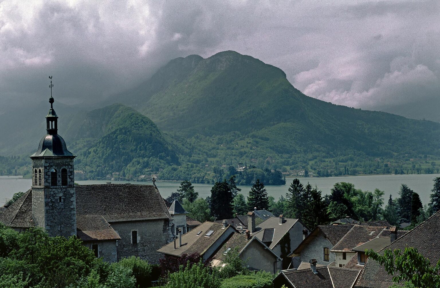 TOWN of TOLLORIES WITH CHURCH STEEPLE  on LAKE ANNECY with WHITE CLOUDS - ALPS REGION, FRANCE
