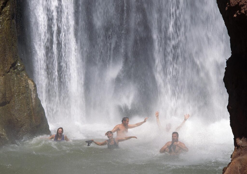 Friends frolic in the powerful downpour of  DEER CREEK FALLS at Mile 136 - GRAND CANYON NATIONAL PARK, ARIZONA (MR)