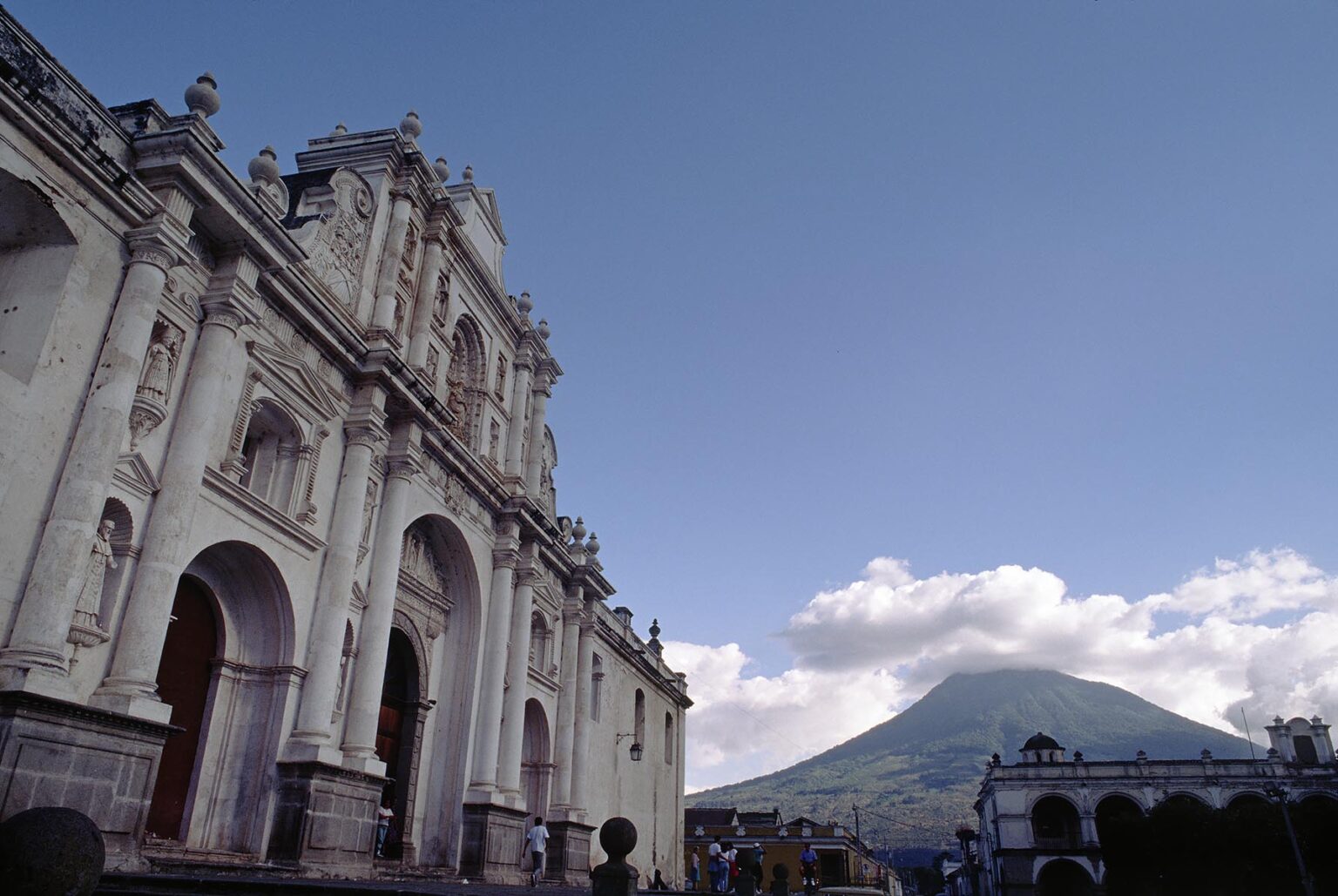 White CATHOLIC CHURCH in the main plaza with VOLCANO in distance - ANTIGUA, GUATEMALA
