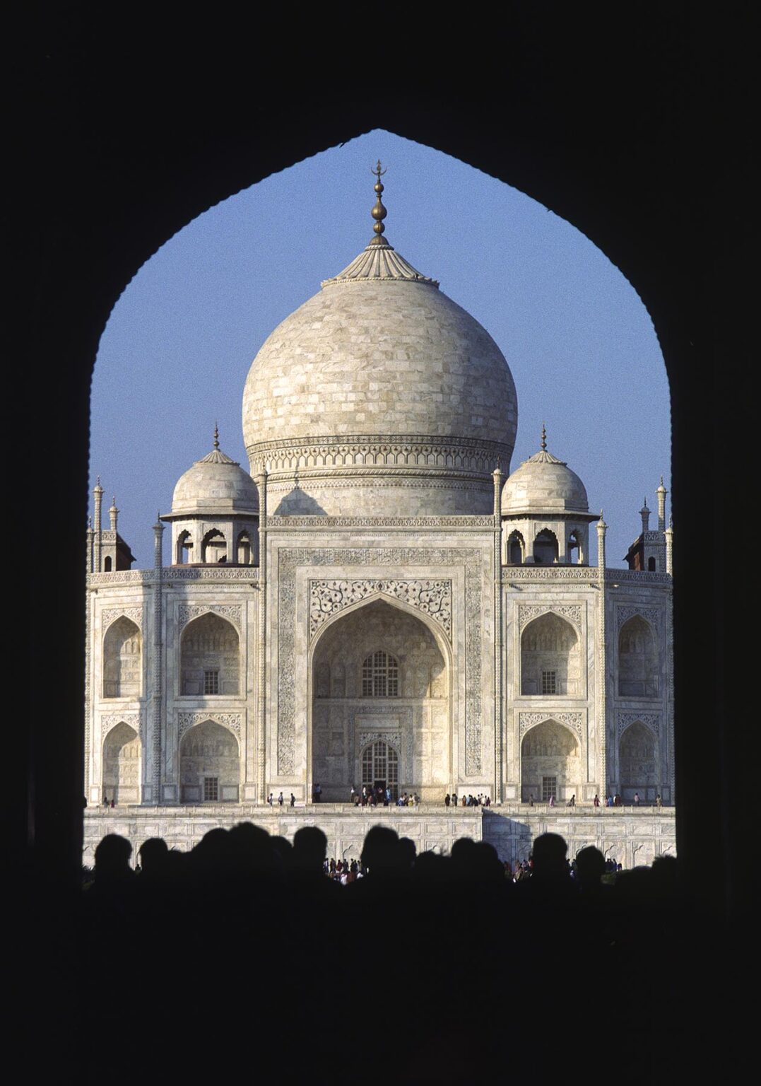 The TAJ MAHAL, built in 1653, is seen over tourist heads from under an ISLAMIC ARCH - AGRA, INDIA
