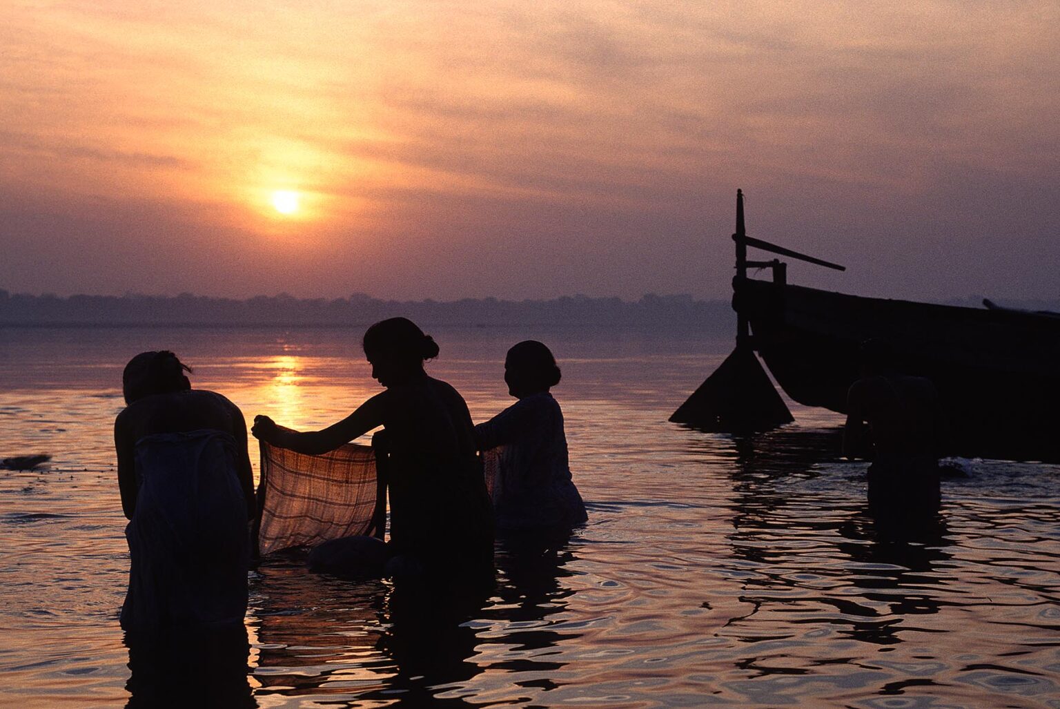 Faithful HINDU WOMEN wash clothes and perform ablutions in the GANGES RIVER at SUNRISE - VARANASI (BENARES), INDIA