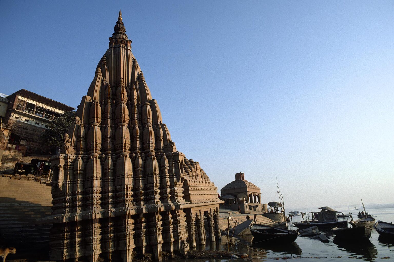 A HINDU TEMPLE rises above CANOES on the GANGES RIVER - VARANASI (BENARES), INDIA