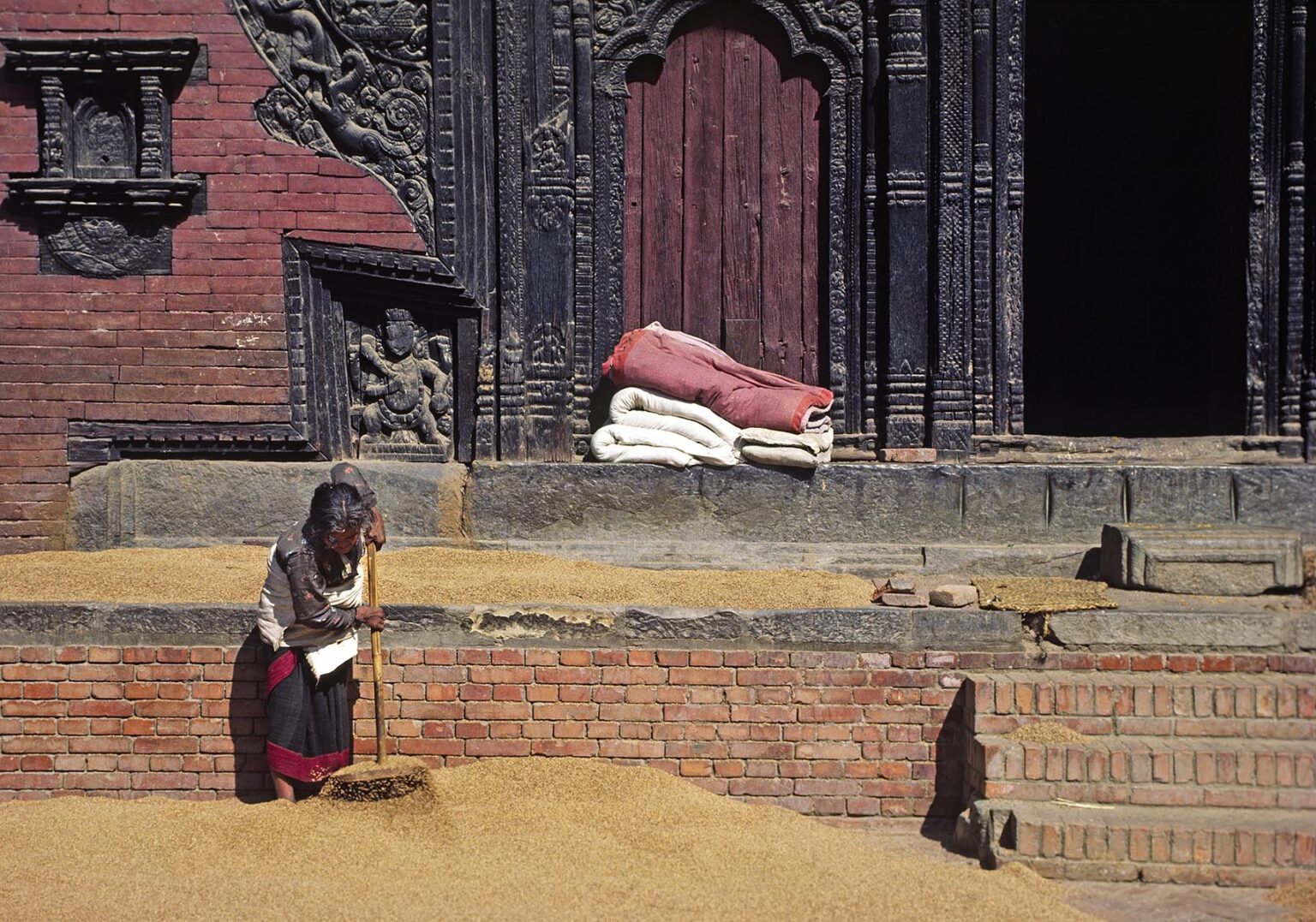 A NEPALI WOMAN rakes RICE drying in a courtyard - KATHAMANDU, NEPAL