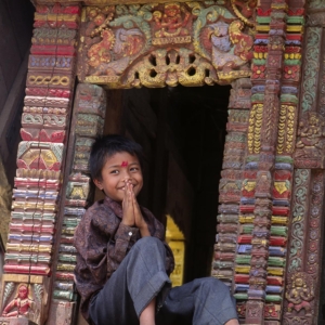 A boy signs NAMASTE meaning I salute the God within You, as he sits in a CHARIOT used in a local festival - BHAKTAPUR, NEPAL