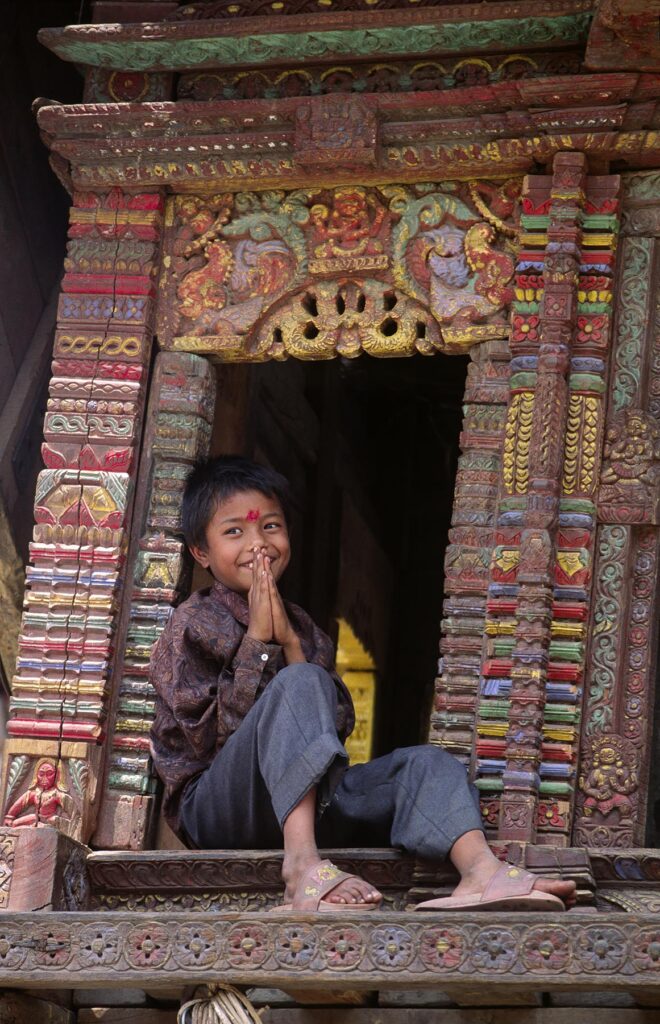 A boy signs NAMASTE meaning I salute the God within You, as he sits in a CHARIOT used in a local festival - BHAKTAPUR, NEPAL