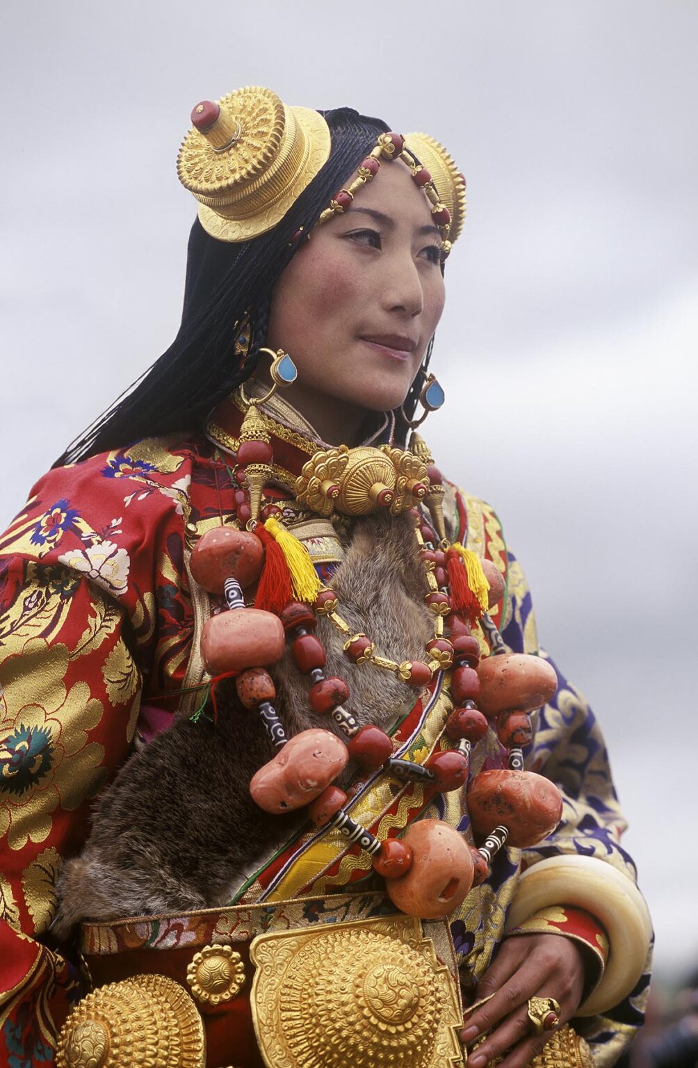Female Khampa wears gold hair pieces and gau boxes, zee stones & coral at the Litang Horse Festival - Sichuan Province, China