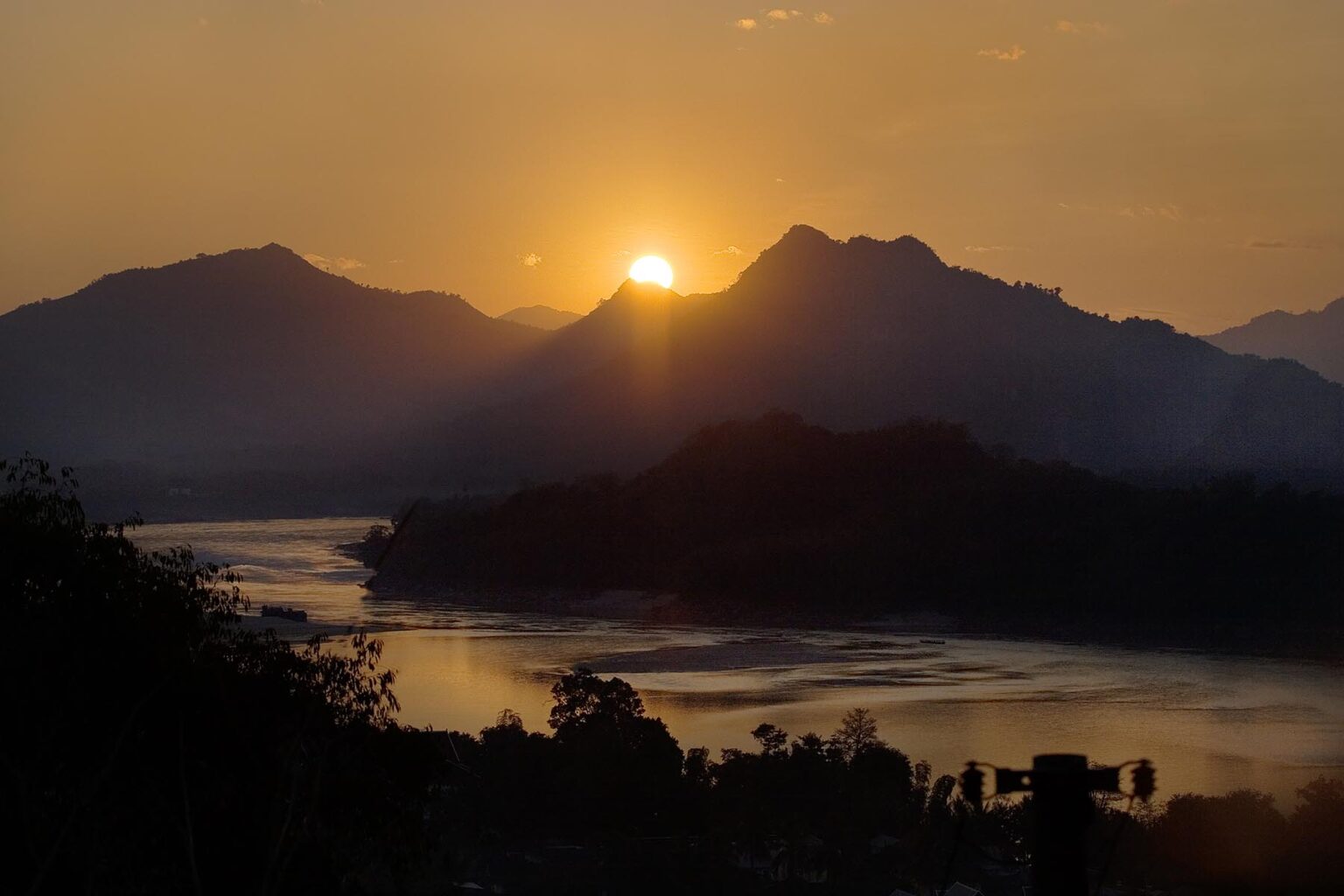 The sun sets over a hill on the Mekong River in the former Provincial town of LUANG PROBANG - LAOS