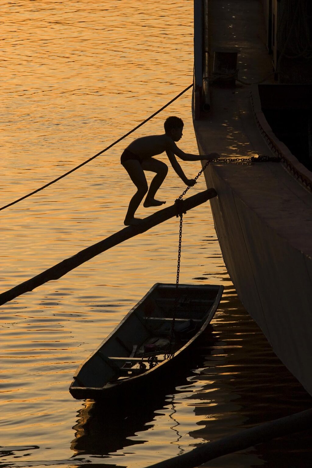 Young boy walks up a plank to a boat on the Mekong River at dusk - LUANG PROBANG, LAOS