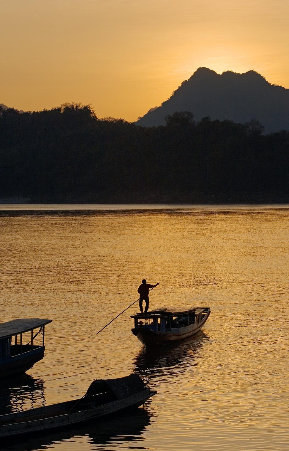 The sunsets on the Mekong River silhouetting a slow boat which is used for transportation - LUANG PROBANG, LAOS