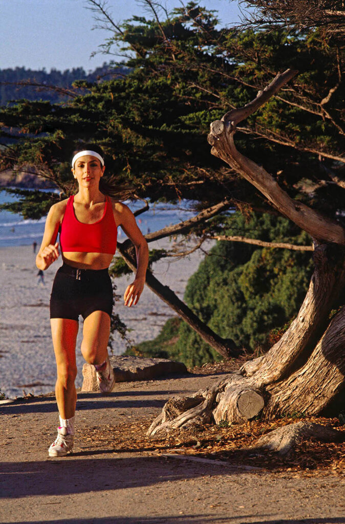 A lifestyle image of a woman jogging along the beach in Carmel California.  Lifestyle photography by Craig Lovell