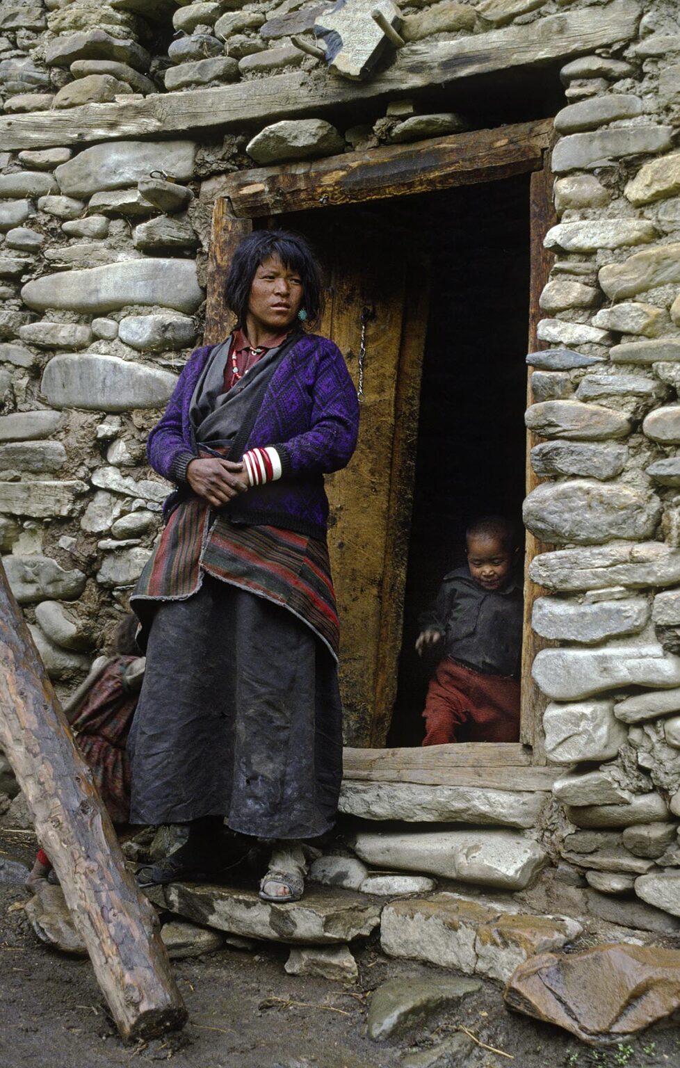 NEPALI MOTHER and CHILD stand in front of a traditional mud and stone HOUSE in the upper DO TARAP VALLEY - DOLPO, NEPAL