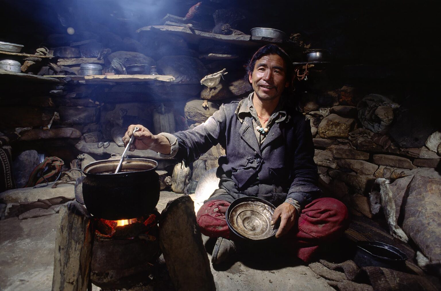 A DOLPO MAN COOKING FOOD with KITCHEN UTENSILS in a yak herder hut - DOLPO DISTRICT, NEPAL