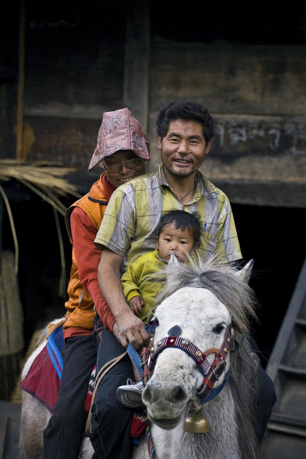 A monk rides a horse with a father and son in BIHI in the Buddhist area of NUPRI - AROUND MANASLU TREK, NEPAL