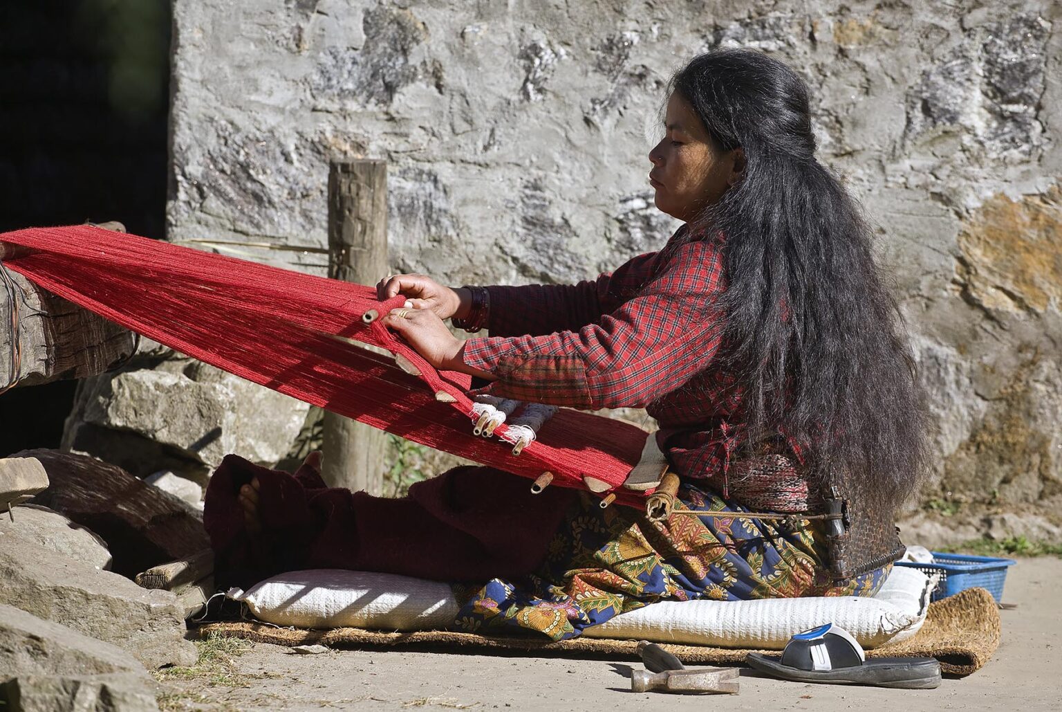 A tribal woman uses a BACKSTRAP LOOM to make red cloth in GYASUMDO VILLAGE near Manang on the ANNAPURNA CIRCUIT - NEPAL HIMALAYA