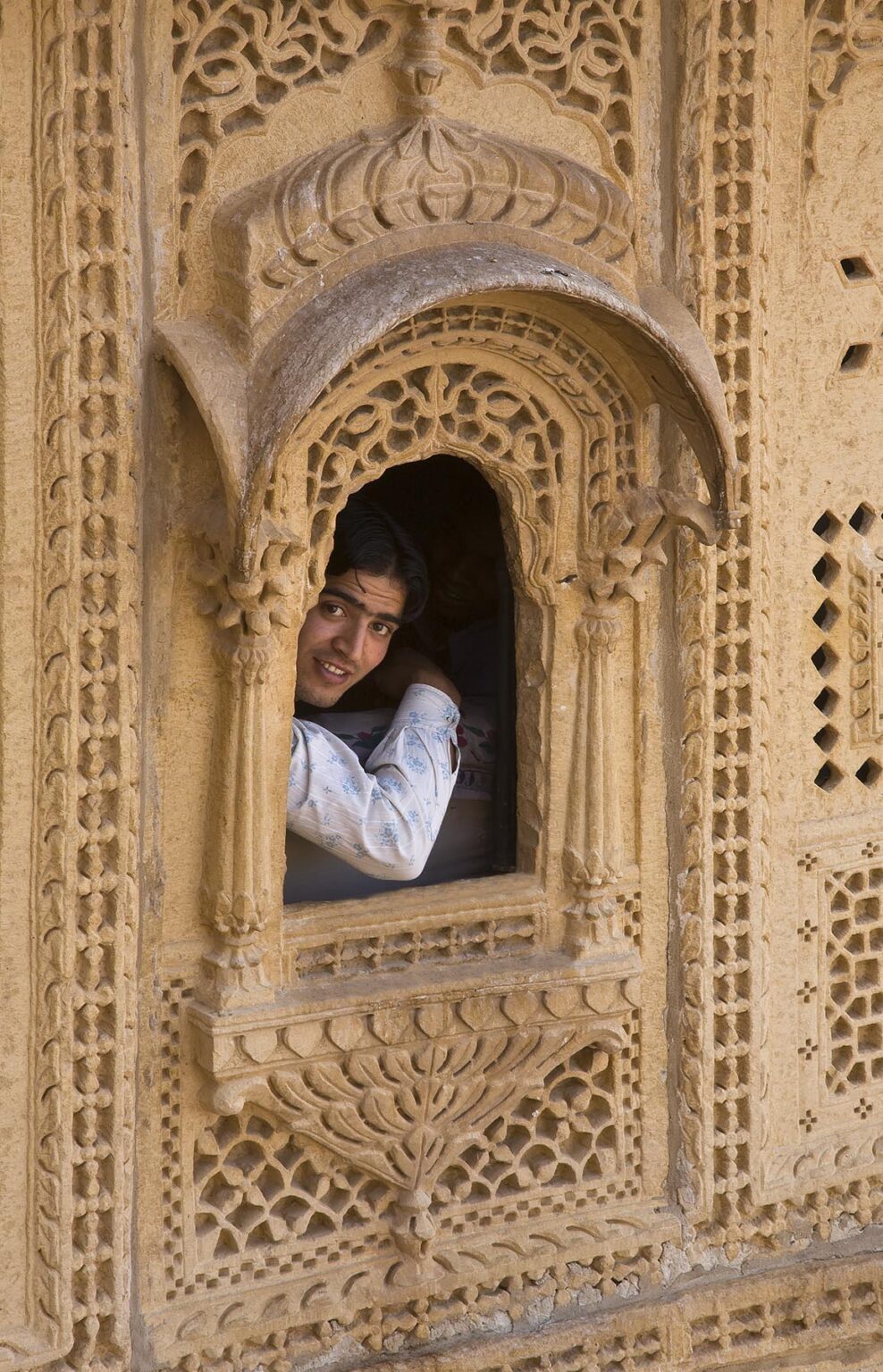 An Indian boy looks out a hand carved sandstone WINDOW in the MAHARAJA'S PALACE located inside JAISALMER FORT - RAJASTHAN, INDIA