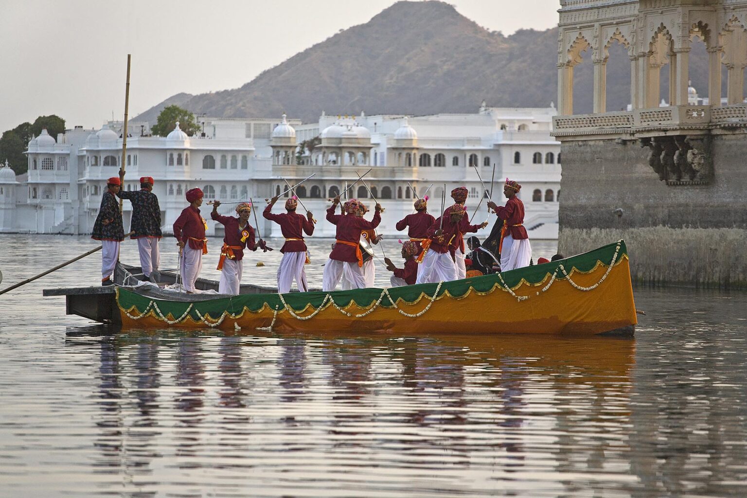 Rajasthani men dance with swords on a boat on LAKE PICHOLA during the GANGUR FESTIVAL or MEWAR FESTIVAL - UDAIPUR, RAJASTHAN, INDIA