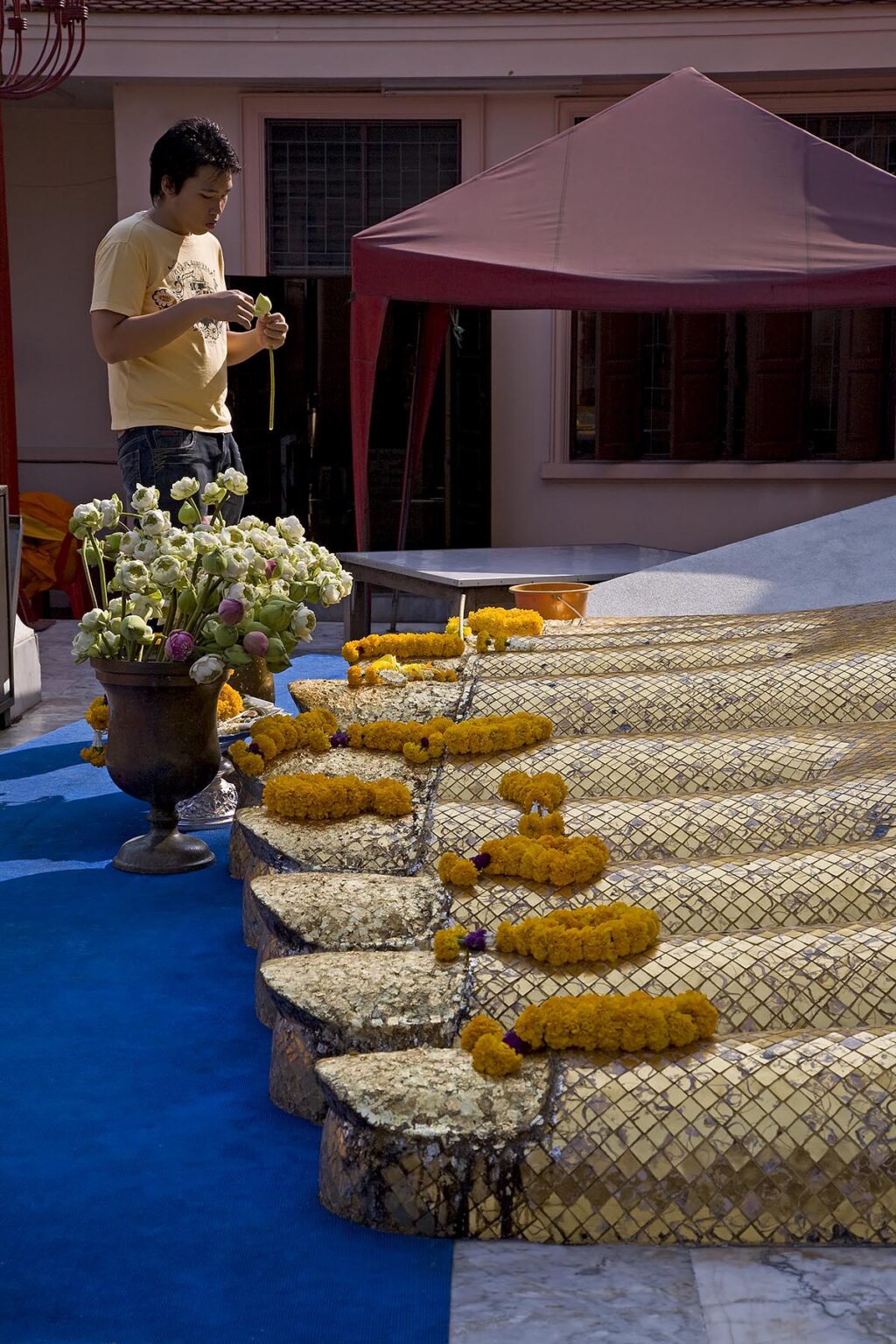 Flower offerings at the FEET of the GIANT STANDING BUDDHA (32 meters) known as LUANG PHO TO at the Theravada Buddhist Temple of WAT INTHARAVIHAN - BANGKOK, THAILAND