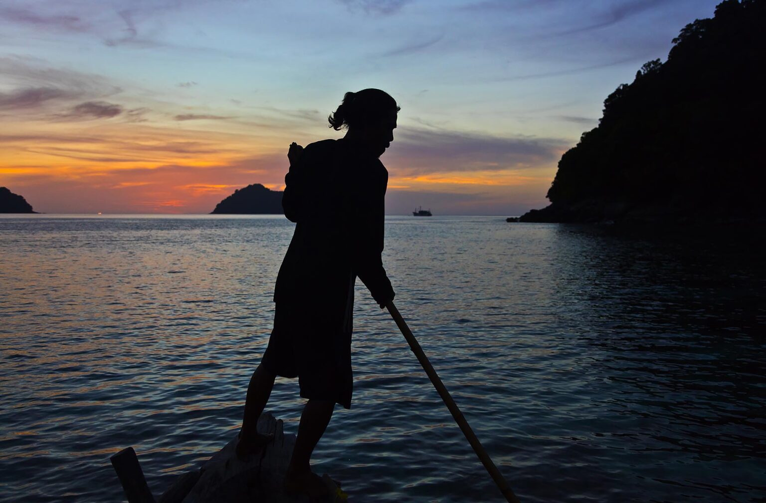 A MOKEN MAN steers his boat at sunsets on KO SURIN THAI ISLAND in MU KO SURIN NATIONAL PARK - THAILAND