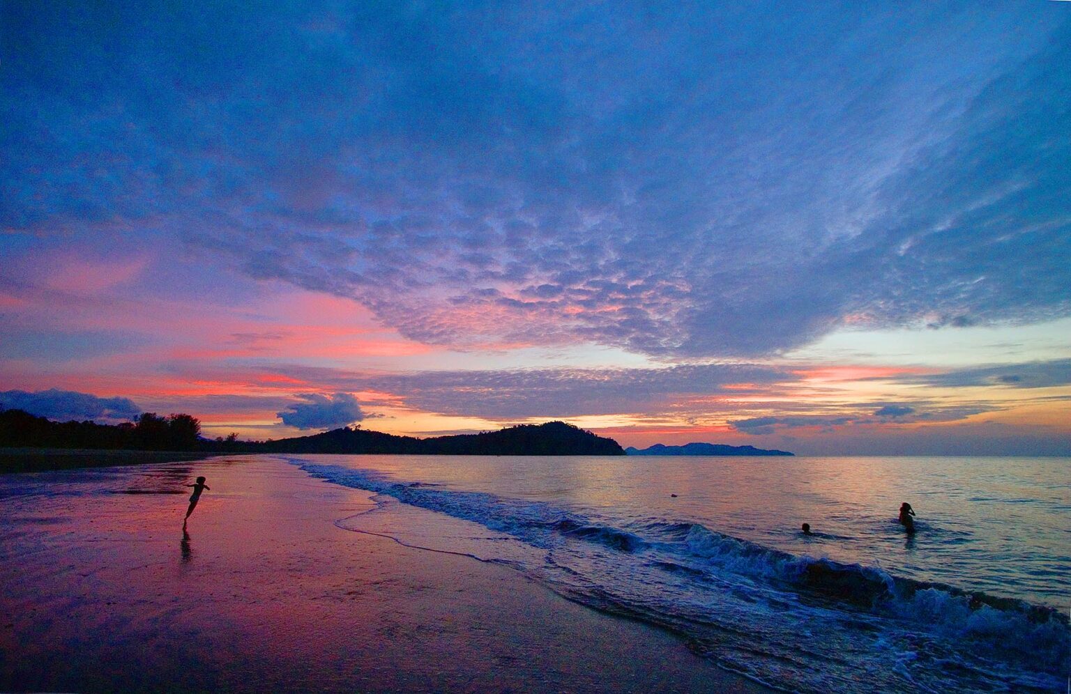 Sunset over the North Andaman Sea silhouettes children playing in the surf at Hat Prapat Beach - KURABURI, THAILAND