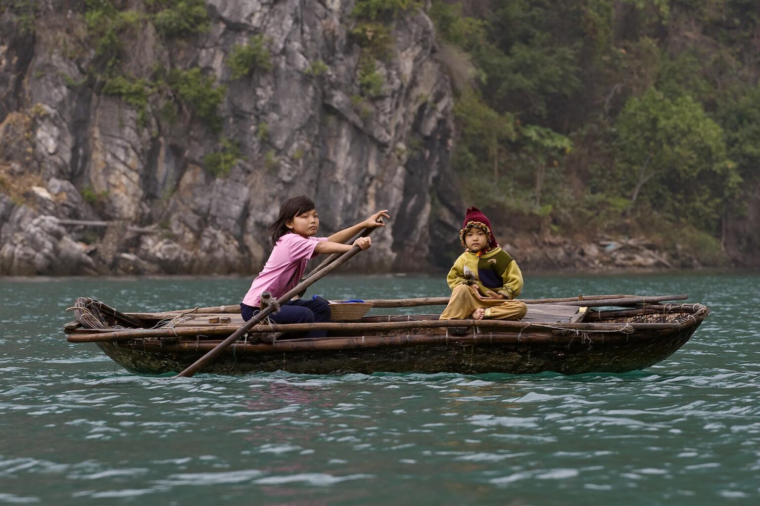 A young VIETNAMESE girl rows her sister in a small boat on the waters of HALONG BAY - VIETNAM
