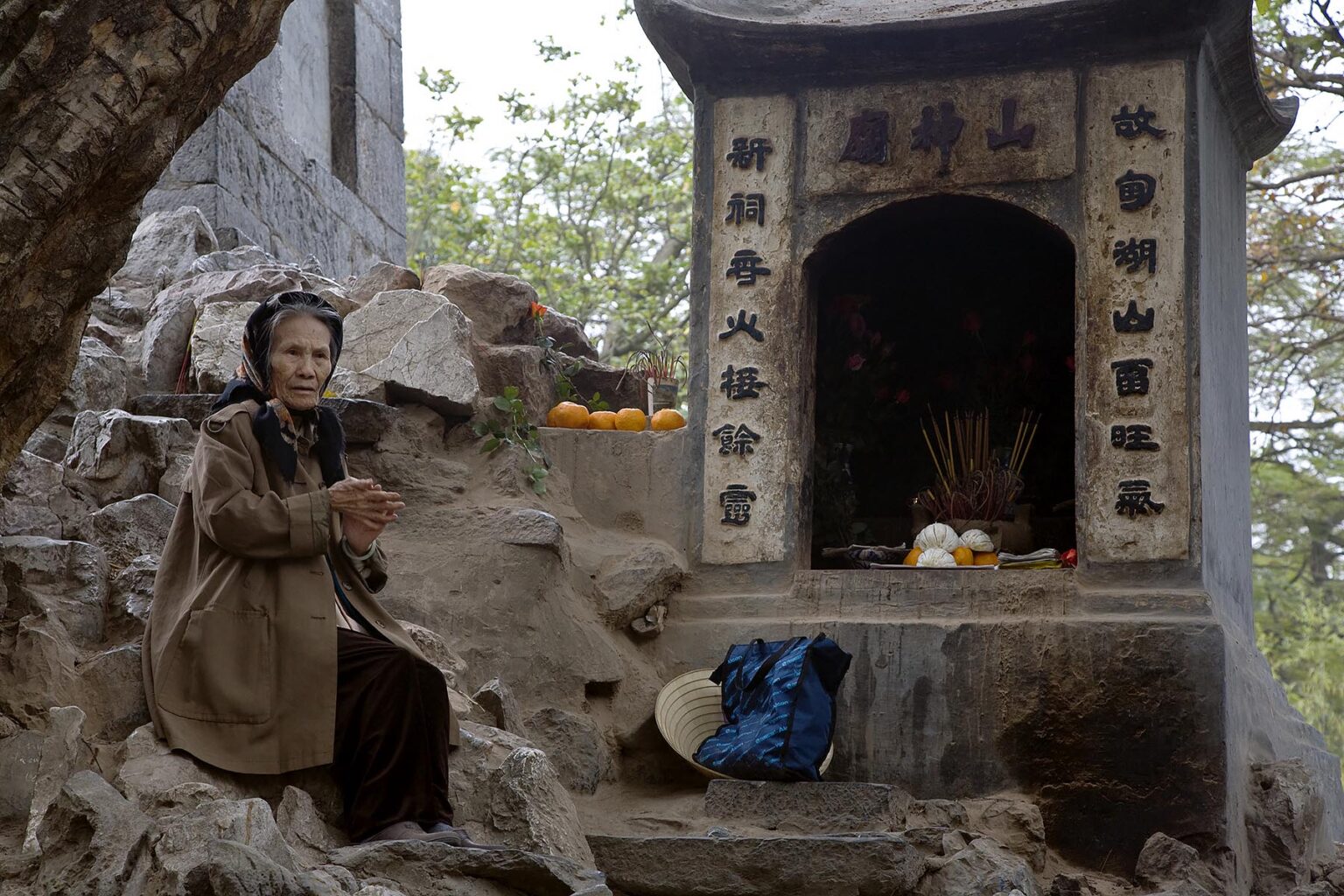 An elderly VIETNAMESE woman sits at the base of the NGOC SON TEMPLE in the old quarter - HANOI. VIETNAM