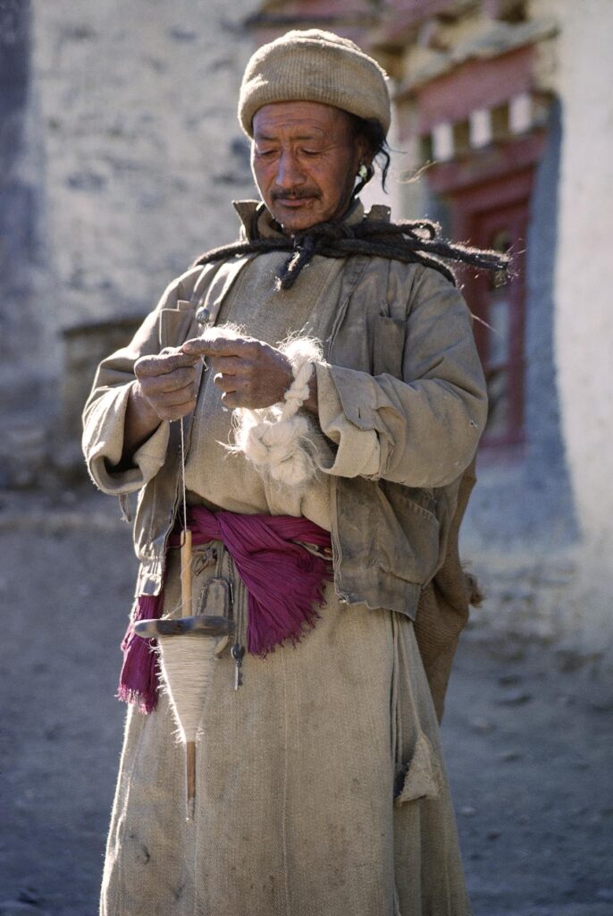 LADAKHI MAN in traditional chuba spinning YARN from sheep's wool with a DROP SPINDLE, LAMAYURU - LADAKH, INDIA