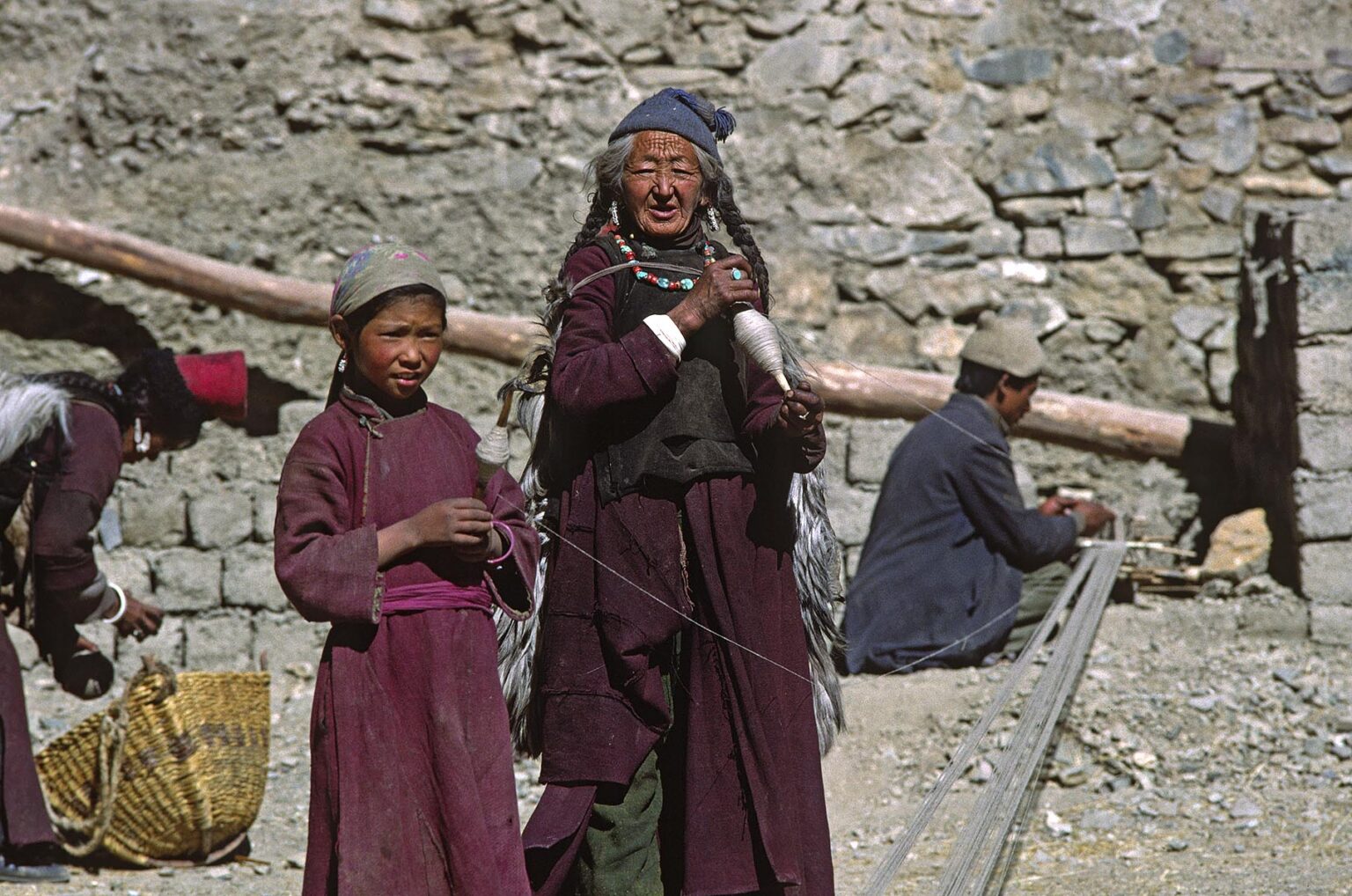 LADAKHI WOMEN wearing HATS and turquoise and coral necklaces preparing a loom to make cloth in LAMAYURU village - LADAKH, INDIA
