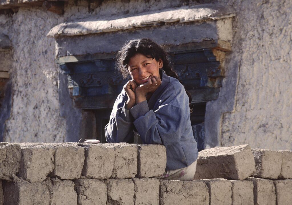 Beautiful SMILING LADAKHI GIRL (young woman) sitting on ADOBE BRICKS - LADAKH, INDIA