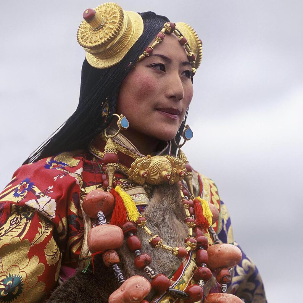 Female Khampa wears gold hair pieces & gau boxes, zee stones & coral at the Litang Horse Festival - Sichuan Province, China