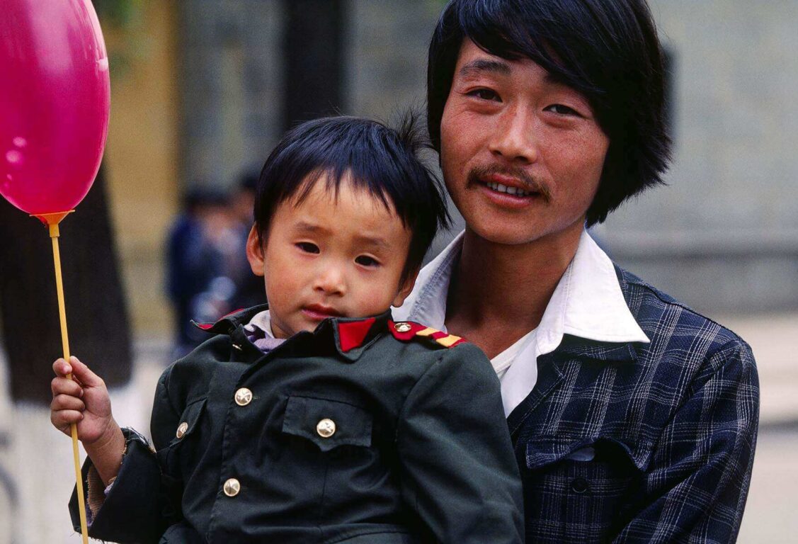 A CHINESE MAN carries his son who has a baloon on the streets of KUNMING - YUNNAN, CHINA