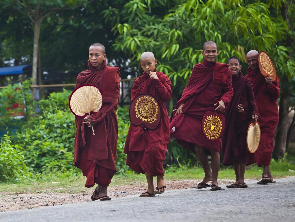 BUDDHIST MONKS with fans walk along the road - BAGO, MYANMAR