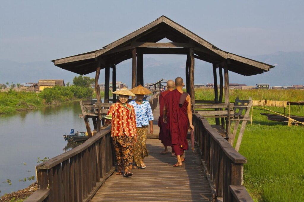 BURMESE WOWMEN and BUDDHIST MONKS use the raised walkway near the village of MAING THAUK on the way to the weekly market - INLE LAKE, MYANMAR