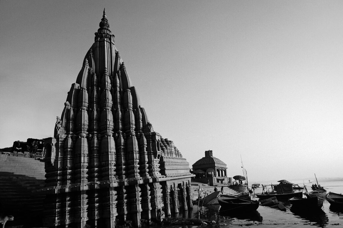 A HINDU TEMPLE rises above CANOES on the GANGES RIVER - VARANASI (BENARES), INDIA