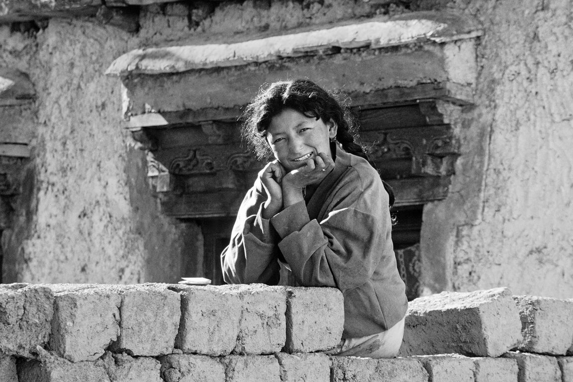Beautiful SMILING LADAKHI GIRL (young woman) sitting on ADOBE BRICKS - LADAKH, INDIA