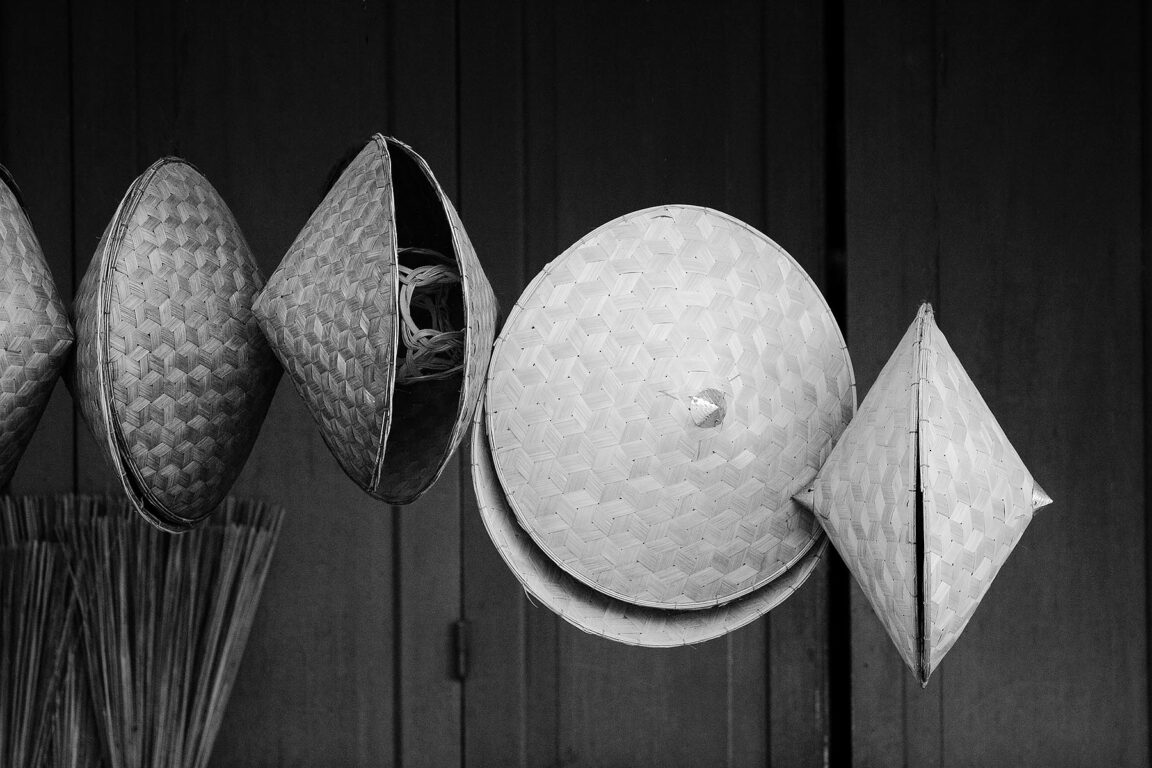 Hand woven rattan hats hang in a shop - LUANG PROBANG, LAOS